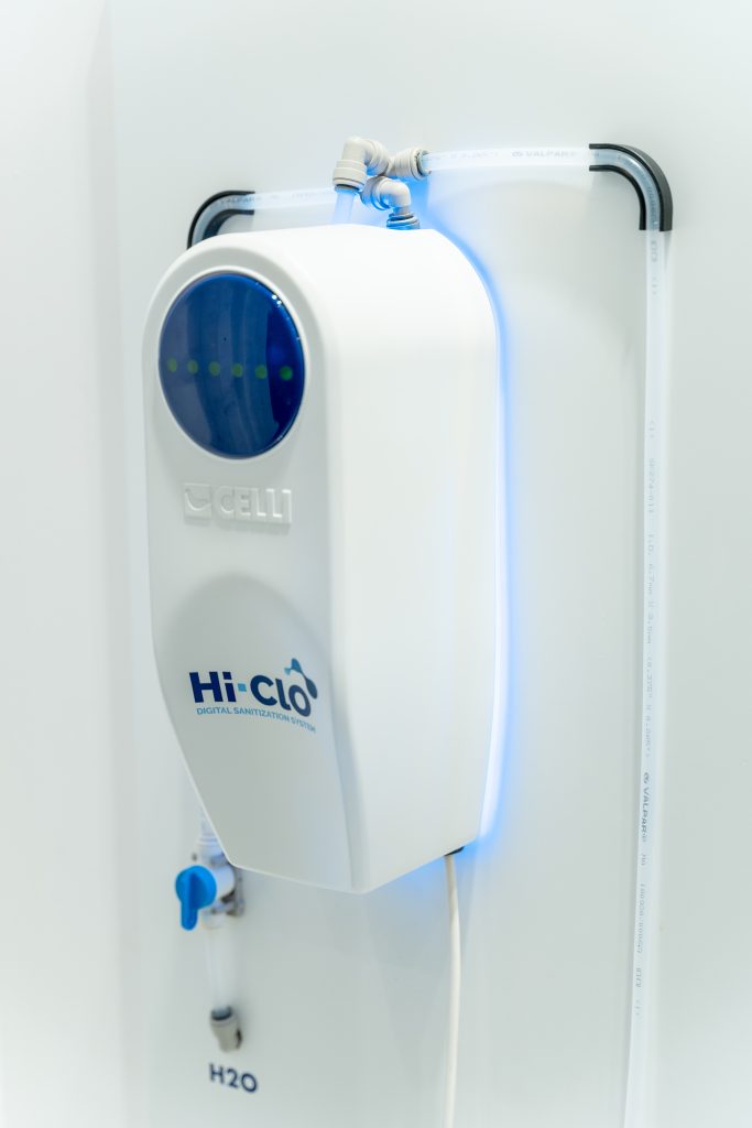 Hi-ClO device, white box with leds on the upper part and water and sanitizer inlet and outlet pipes
